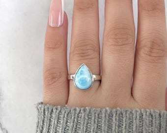 May include: A silver ring featuring a pear-shaped, light blue gemstone with white marbling. The ring is set in a simple, polished silver band. The gemstone is approximately 0.75 inches in length.