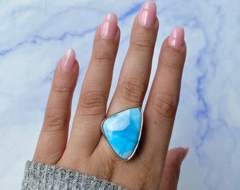 May include: A silver ring featuring a large, triangular-shaped stone with a smooth, polished surface. The stone displays a vibrant sky-blue color with white, cloud-like veining patterns throughout. The metal setting is simple and polished.