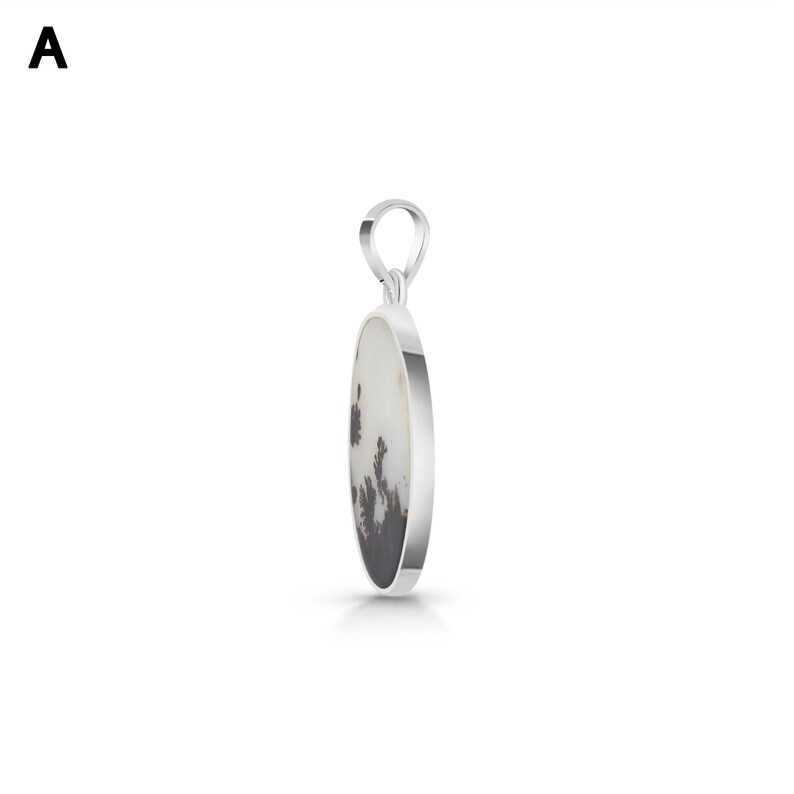 Puede incluir: Un colgante de plata con una piedra ovalada de base blanca e inclusiones dendr&iacute;ticas oscuras en forma de &aacute;rbol. La piedra est&aacute; engastada en un marco de plata pulida lisa con una anilla de plata a juego en la parte superior para la cadena.