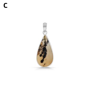 Puede incluir: Un colgante en forma de l&aacute;grima con una piedra beige e inclusiones dendr&iacute;ticas negras, engastado en un marco de metal plateado con una anilla a juego. La letra C es visible en la esquina superior izquierda de la imagen.