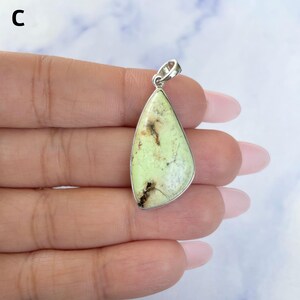 Pu&ograve; includere: Un ciondolo a forma di goccia con una pietra verde pallido e inclusioni di matrice marrone scuro, incastonato in una montatura in metallo color argento lucido con un piccolo occhiello circolare sulla parte superiore per una catenina.
