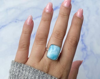 May include: A silver ring featuring a large, rectangular, polished light blue stone with white marbled patterns. The stone is set in a smooth metal bezel, and the band is a simple, polished silver metal. The letter A is visible in the top corner.