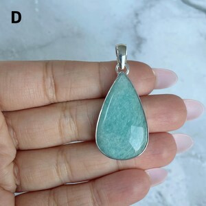 May include: A teardrop-shaped pendant featuring a smooth, light green gemstone set in a polished silver-toned metal frame. The pendant includes a small silver-toned bail at the top for attachment to a chain. The letter D is visible in the corner.
