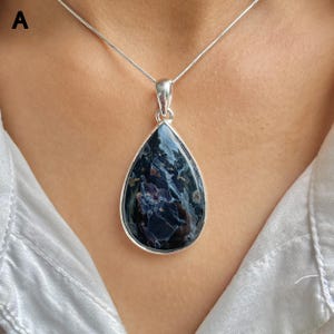 May include: A teardrop-shaped pendant necklace featuring a dark blue and black patterned gemstone set in a polished silver frame. The pendant hangs from a thin silver chain, showcasing deep indigo and charcoal swirls within the stone's surface.