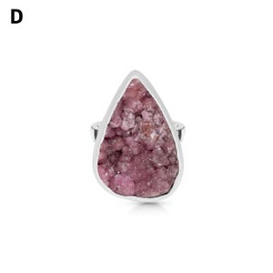 May include: A silver ring featuring a large, teardrop-shaped pink gemstone. The gemstone has a textured, crystalline appearance and is set in a polished silver band. The ring is displayed against a white background.