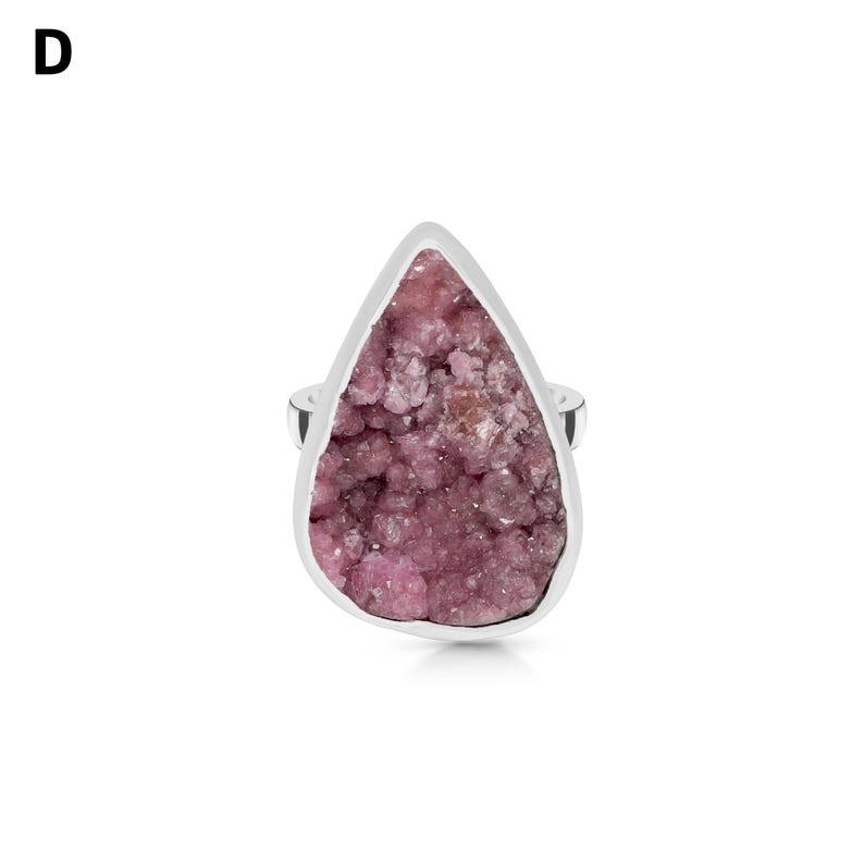 May include: A silver ring featuring a large, teardrop-shaped pink gemstone. The gemstone has a textured, crystalline appearance and is set in a polished silver band. The ring is displayed against a white background.
