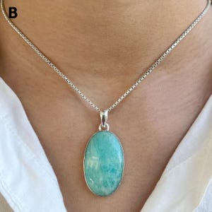 May include: A silver box chain necklace featuring a large, smooth, oval-shaped cabochon pendant in a pale turquoise-green color. The pendant is set in a simple silver frame with a small bail connecting it to the metallic chain.