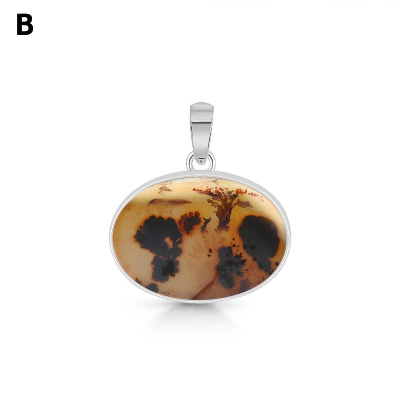 Puede incluir: Un colgante ovalado con una piedra pulida de color tostado claro con inclusiones dendr&iacute;ticas de color marr&oacute;n oscuro en forma de &aacute;rbol. La piedra est&aacute; engastada en un bisel de metal plateado liso con una anilla plateada a juego. La letra B es visible.