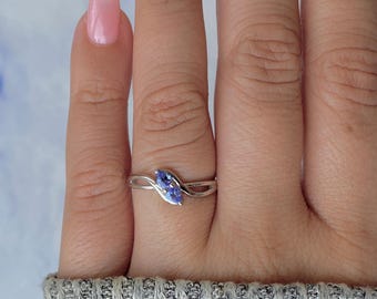 May include: A silver ring with a marquise-cut, light purple gemstone. The ring's band has a delicate, swirling design. The ring is shown on a person's finger, showcasing the jewelry's elegant style.