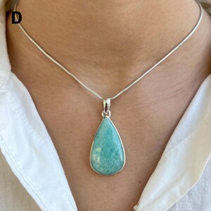 May include: A silver necklace featuring a teardrop-shaped pendant with a smooth, opaque light blue-green stone set in a polished silver frame. The pendant hangs from a thin, flexible silver snake chain that rests against the collarbone area.