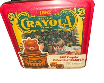 May include: A red metal tin with a 1992 Crayola logo and a Christmas scene featuring a teddy bear, a Christmas tree, and two children. The tin includes a dated nostalgic tin, first in a series, and exclusive Crayola crayons.