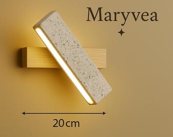 May include: A modern wall sconce with a rectangular, speckled, light gray shade and a warm, glowing light. The sconce is mounted on a wooden base. The text "Maryvea" is displayed above the sconce. The sconce is 20 cm long.