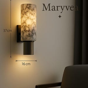 Puede incluir: Una lámpara de pared de mármol blanco y negro con una base de metal dorado. La lámpara tiene 37 cm de alto y 16 cm de ancho. La lámpara está encendida y proyecta una luz cálida. El texto "Maryvea" es visible en la imagen.