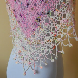 May include: A white crochet shawl with a pink and white ombre design and a fringe border. The shawl is made with a delicate stitch pattern and has a light and airy feel.