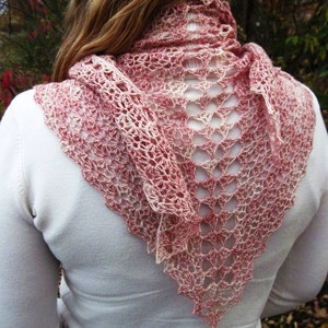 May include: A pink and white crocheted shawl with a delicate lace pattern. The shawl is draped over the shoulders of a person wearing a white sweater.