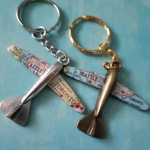 May include: Two silver and bronze airplane keychains with map details. The silver keychain has the text "SEATTLE" and "TORONTO" on it. The bronze keychain has the text "SEATTLE" and "TORONTO" on it.