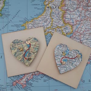 May include: Two heart-shaped map ornaments with red lines and gold stars. The maps are of the United Kingdom and feature the text "Salisbury" and "Charlotte".