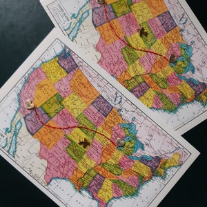 May include: Two vintage maps of the United States with red lines and gold heart-shaped pins marking a route across the country.