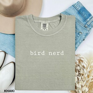 May include: Khaki green t-shirt with the text "bird nerd" printed in white on the front. The shirt is made of a soft, comfortable fabric.