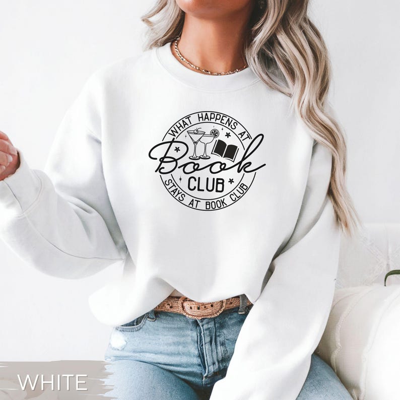 May include: White sweatshirt with a black graphic that reads "What Happens at Book Club Stays at Book Club." The design includes a cocktail glass, a book, and stars. The sweatshirt is a long-sleeved crew neck.