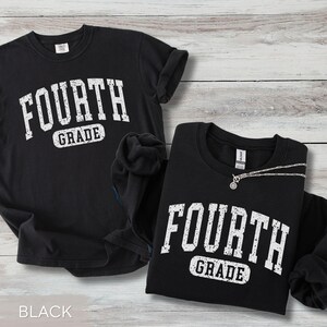 May include: A black short-sleeved t-shirt and a black long-sleeved sweatshirt, both featuring the white distressed text "FOURTH GRADE" printed in a collegiate font. The garments are displayed together, showcasing the matching graphic design.