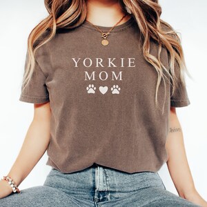 May include: A brown t-shirt with the text "Yorkie Mom" and two paw prints and a heart in white.
