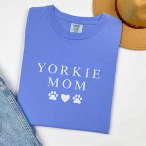 May include: A light blue t-shirt with the text "Yorkie Mom" in white lettering and two white paw prints and a white heart.