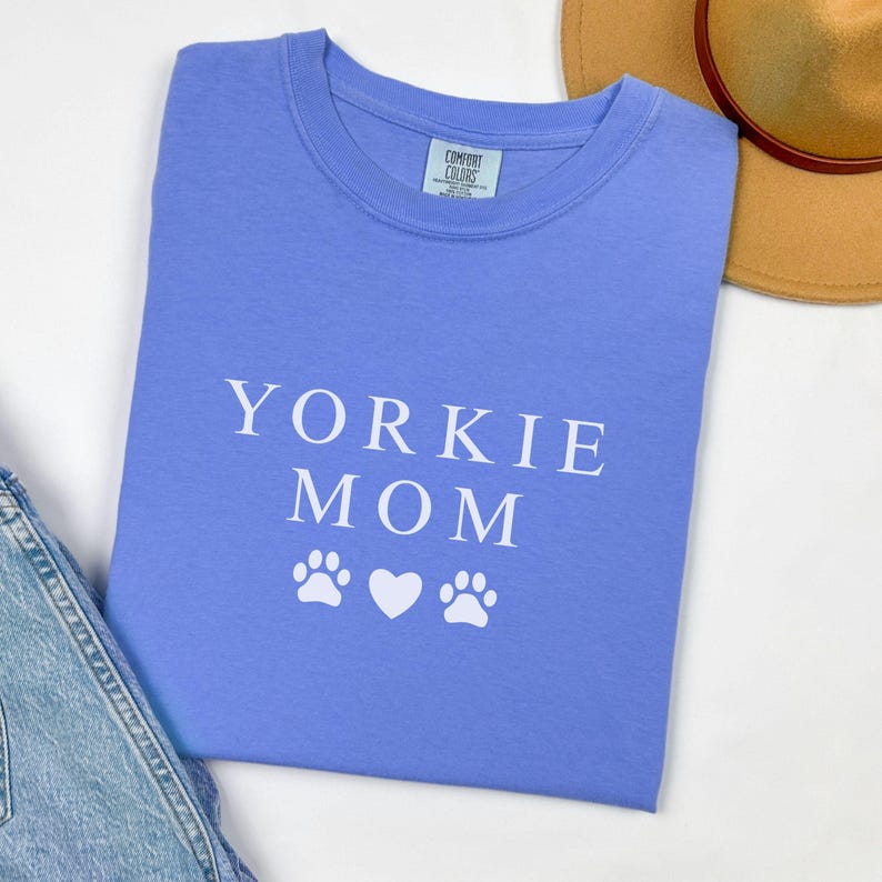 May include: A light blue t-shirt with the text "Yorkie Mom" in white lettering and two white paw prints and a white heart.