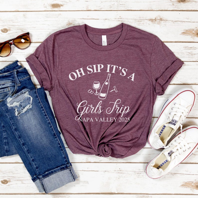 May include: A maroon t-shirt with the text "Oh Sip It's a Girls Trip Napa Valley 2025" and a graphic of a wine bottle, wine glass, and corkscrew.
