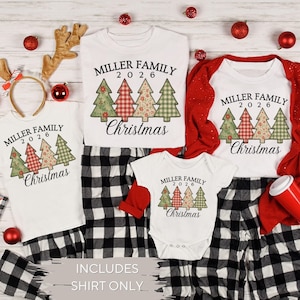 May include: Three white t-shirts and one white baby bodysuit featuring the text Miller Family 2026 Christmas and four patterned Christmas tree graphics. The garments are displayed alongside black and white plaid fabric and red ornaments.