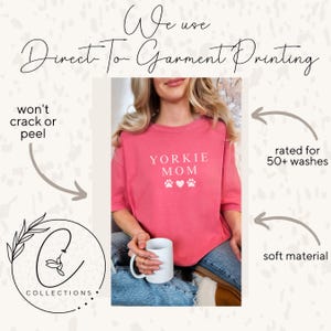 May include: A pink t-shirt with the text "YORKIE MOM" in white, featuring paw prints and hearts. The shirt is made with a soft material and is rated for 50+ washes.