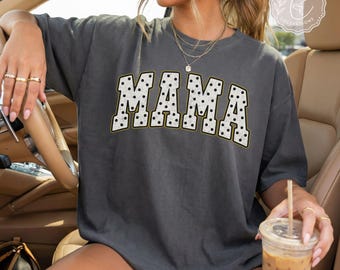 May include: A charcoal gray short-sleeve t-shirt featuring the word MAMA in a large, arched, white collegiate-style font with black polka dots. The shirt has a crew neckline and a relaxed fit, with a logo in the top right corner.