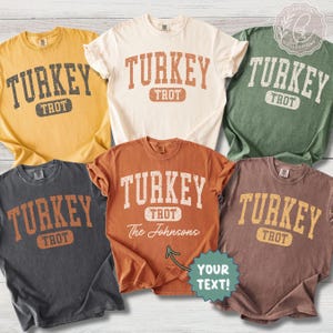 May include: A collection of five short-sleeve t-shirts in yellow, cream, green, dark grey, and rust orange. Each shirt features the text TURKEY TROT in a distressed collegiate font. One shirt includes the custom text The Johnsons and YOUR TEXT.