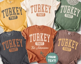 May include: A collection of five short-sleeve t-shirts in yellow, cream, green, dark gray, and rust orange. Each shirt features the text TURKEY TROT in a distressed collegiate font. One shirt includes the custom text The Johnsons and YOUR TEXT.