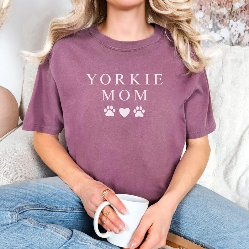 May include: A mauve colored t-shirt with the text "Yorkie Mom" and two paw prints and a heart in white.