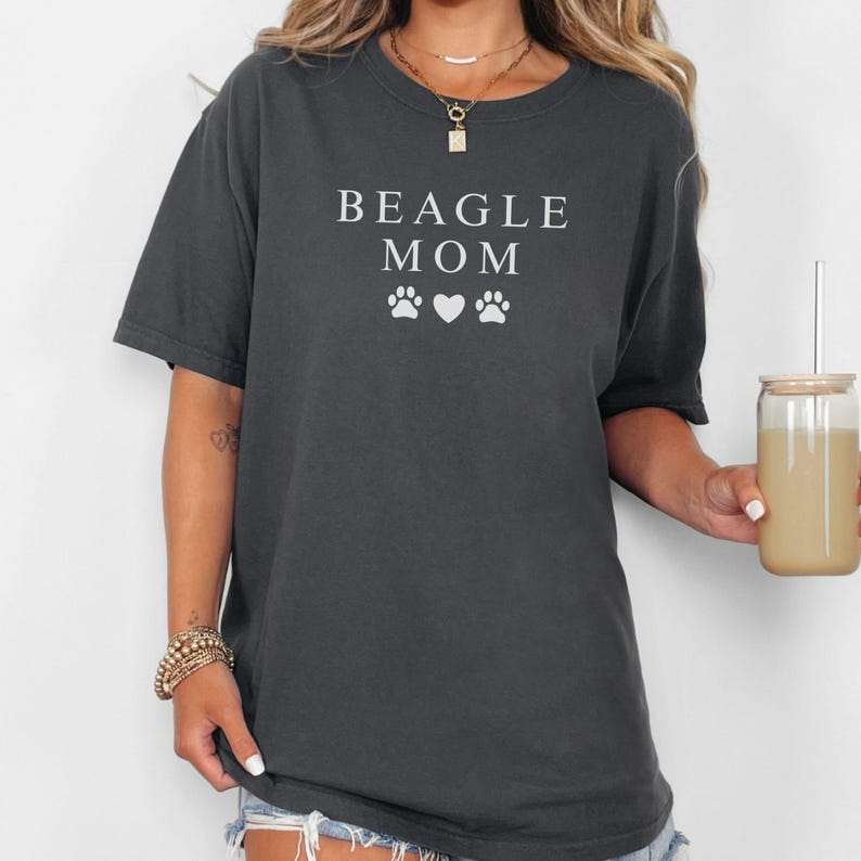 K&ouml;nnte beinhalten: Ein dunkelgraues T-Shirt mit dem Text "BEAGLE MOM" und zwei wei&szlig;en Pfotenabdr&uuml;cken und einem Herzen auf der Vorderseite.