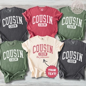 May include: Five short-sleeved crew neck t-shirts in charcoal, red, olive green, and cream colours. Each shirt features the distressed white or red text COUSIN CREW. The cream shirt includes the text the johnsons and YOUR TEXT!.
