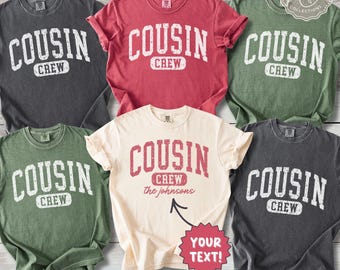 May include: Five short-sleeved crew neck t-shirts in charcoal, red, olive green, and cream colors. Each shirt features the distressed white or red text COUSIN CREW. The cream shirt includes the text the johnsons and YOUR TEXT!.