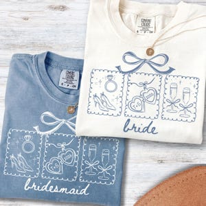 May include: Two Comfort Colors t-shirts, one in blue and one cream, with wedding graphics. The blue shirt says "bridesmaid" and the cream shirt says "bride". Each shirt has a bow and three framed illustrations: a ring, shoes, hearts, and champagne flutes.
