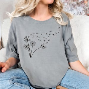 May include: A gray t-shirt with a black dandelion design. The dandelion has seeds blowing in the wind.