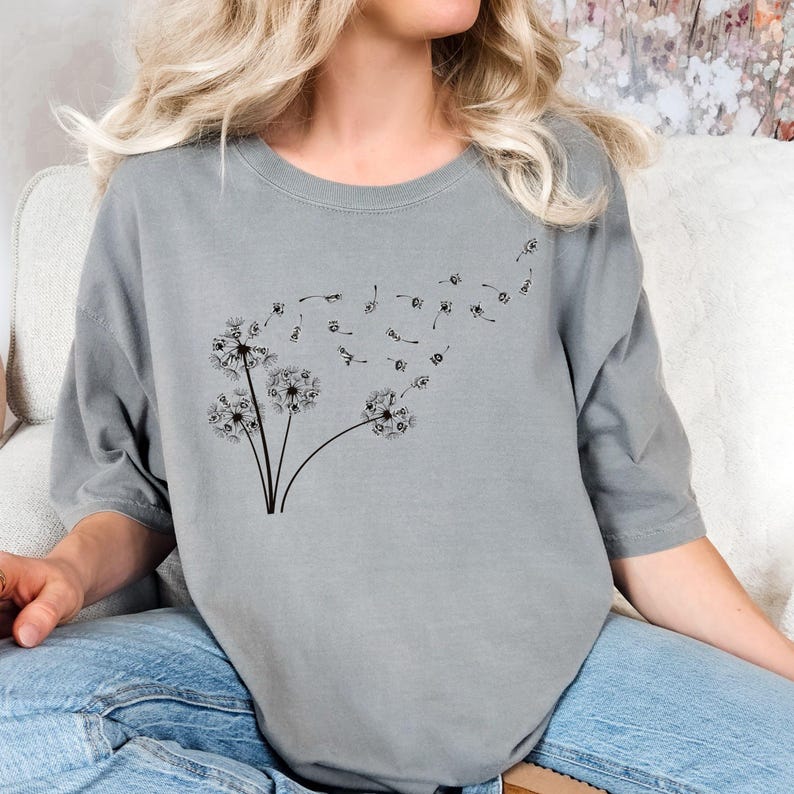 May include: A gray t-shirt with a black dandelion design. The dandelion has seeds blowing in the wind.