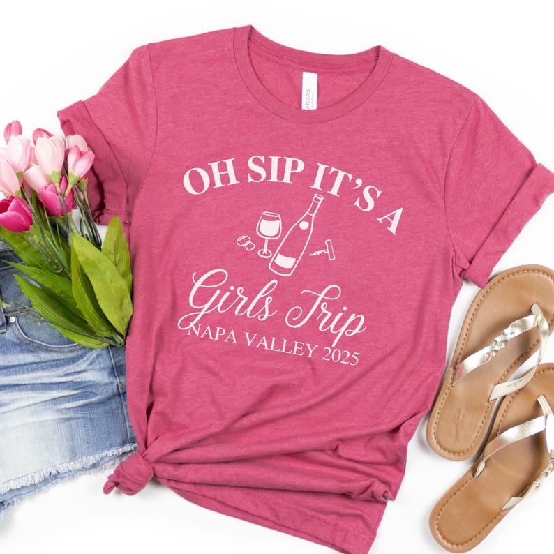 May include: Pink t-shirt with white text that reads "Oh Sip It's a Girls Trip Napa Valley 2025". The shirt also features a graphic of a wine bottle, a wine glass, and a corkscrew.