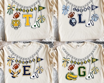 May include: A cream-colored t-shirt featuring a graphic of a silver chain necklace with charms including a bow, a football, a mascot head, a megaphone, a pennant flag with the text GO, and a large varsity letter with the team name spelled out.