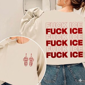 Pode incluir: Um moletom creme com o texto "FUCK ICE" em vermelho repetido nas costas. A frente do moletom apresenta um gr&aacute;fico vermelho de dois dedos m&eacute;dios com as palavras "FUCK ICE".