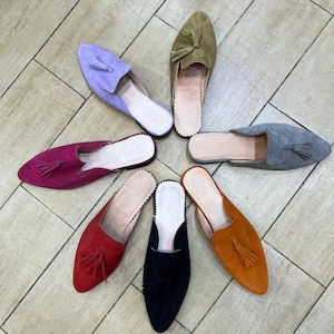 May include: A collection of colorful suede slip-on shoes arranged in a circular pattern. The shoes come in various colors, including purple, olive green, gray, orange, black, red, and fuchsia. Each shoe features a tassel and a leather insole.