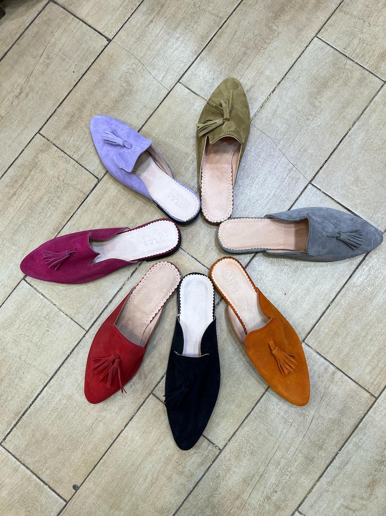May include: A collection of colorful suede slip-on shoes arranged in a circular pattern. The shoes come in various colors, including purple, olive green, gray, orange, black, red, and fuchsia. Each shoe features a tassel and a leather insole.