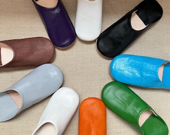 May include: A collection of colorful leather slippers in various hues, including purple, white, black, blue, green, orange, and gray. The slippers are arranged in a circular pattern, showcasing their design and color variations.