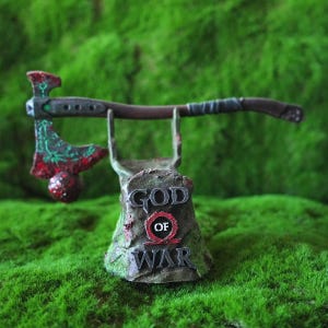 Puede incluir: Una réplica en miniatura del Hacha Leviatán del videojuego God of War. El hacha está montada en un soporte con las palabras "God of War" y el logotipo del juego.