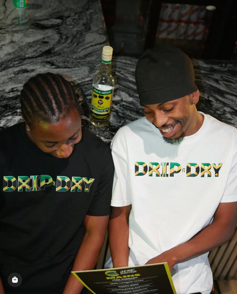 May include: Two people wearing black and white t-shirts with the text "DRIP DRY" in green, yellow, and black. The text is stylized to look like the Jamaican flag.