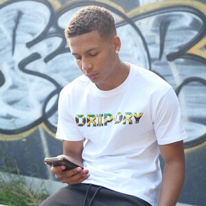 May include: A white t-shirt with the word "DRIPORY" printed in green, yellow, and black letters. The letters are outlined in black and have a Jamaican flag design.
